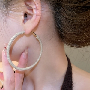 Detailed close-up of gold geometric hoop earrings wrapped in beige leather texture on model
