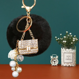 Detail of luxury keychain with black faux fur ball, rhinestone handbag, and pearls