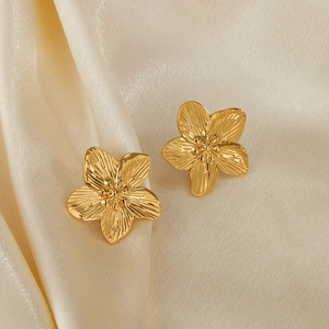 Macro detail of gold-plated five-petal flower earrings with radial textured petals