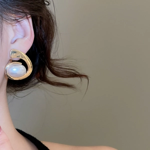Close-up of gold spiral earrings with large oval white pearl on model's ear