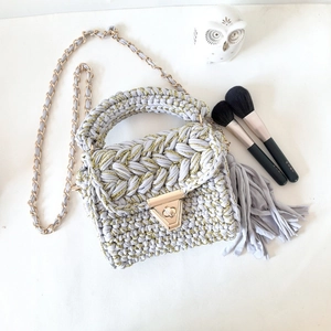 Detail of grey handmade crochet crossbody bag with gold chain strap and elegant tassel decor