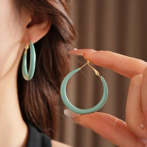 Gros plan de boucles d'oreilles créoles vertes en résine avec clous dorés sur un modèle