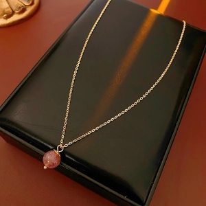 Detail of a gold plated necklace with strawberry quartz pendant on black display box