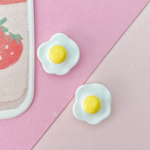 Detailed view of two realistic resin fried egg miniatures for DIY crafts on a pink background