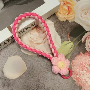 Pink braided flower phone wrist strap with round clasp on a stylish aesthetic background