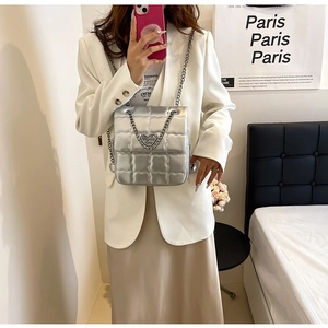 Detail view of silver quilted crossbody bag featuring heart-shaped metal buckle and chain