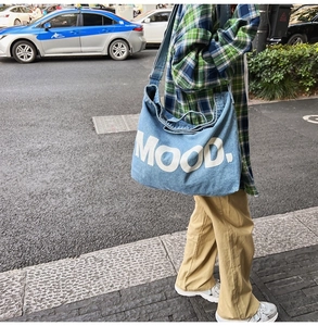 Close-up of light blue denim crossbody bag with MOOD lettering print on a city street