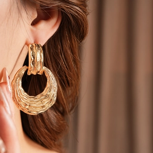 Close-up of a model wearing large textured golden hoop earrings with wavy metal finish