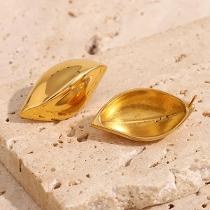 Close-up of golden leaf-shaped stud earrings on a textured stone surface with natural shadows