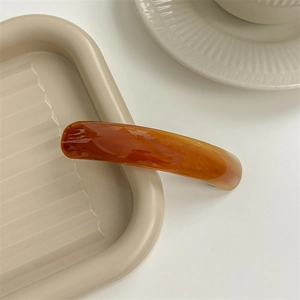 Detailed view of an amber tortoiseshell acetate hair clip on a beige ripple tray