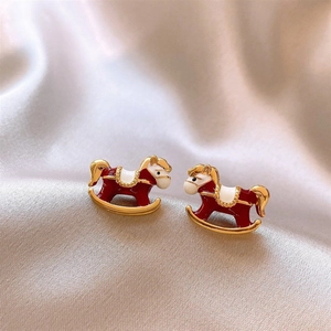 Détail des boucles d'oreilles cheval à bascule en émail rouge et métal doré sur soie