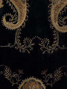 Close-up of golden paisley embroidery and beaded sequins on black velvet fabric