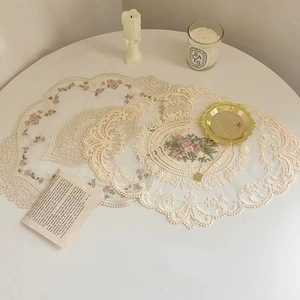 Detail of floral embroidery on beige lace placemat with delicate scalloped edges