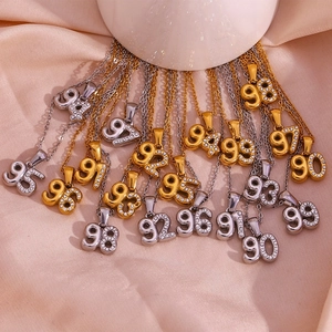Macro shot of 18K gold plated number pendants 90-99 with inlaid zircons on silk fabric