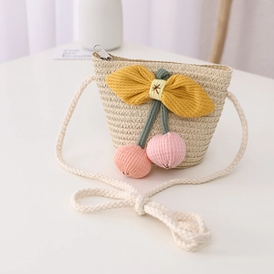 Detail of straw crossbody bag for kids featuring cherry pom-poms and yellow bow decoration