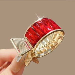 Détail d'une pince à cheveux dorée avec de grands cristaux rouges tenue à la main
