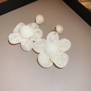 Detail view of woven raffia flower drop earrings with golden metal studs on beige surface