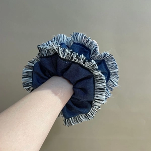 Detail of a large blue denim scrunchie with fringe edges worn on a model's wrist