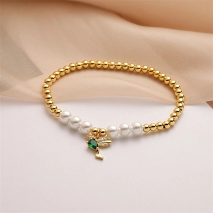 Macro detail of gold beaded bracelet featuring pearl accents and green stone hummingbird charm
