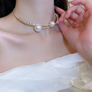Double-layered silver necklace detail with dangling white pearls on a model neck