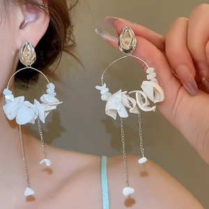 Detail of silver hoop earrings with white shell flowers and long tassels on model