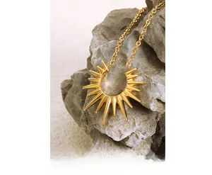 Close-up of a golden sunburst pendant on gray rock, showcasing polished steel texture