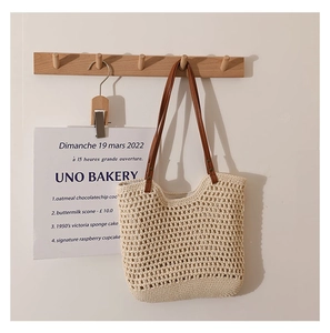 Detail of hollow woven cotton handbag with slim brown leather straps on a wooden hook