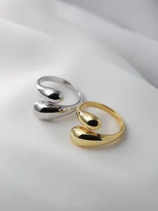 Macro detail of gold and silver teardrop open rings on white silk fabric background