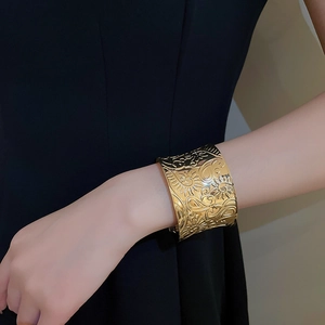 Macro view of wide gold cuff bracelet featuring vintage floral and sunburst relief patterns