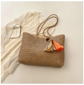 Detailed close-up of straw beach tote bag featuring decorative colorful tassels