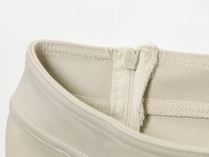 Detailed close-up showing the zipper and waist construction on beige casual trousers