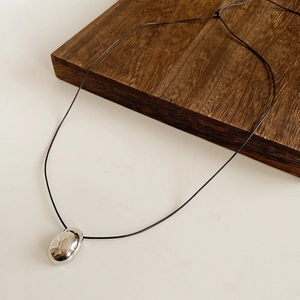 Détail du pendentif ovale argenté avec cordon noir ajustable sur un bloc de bois