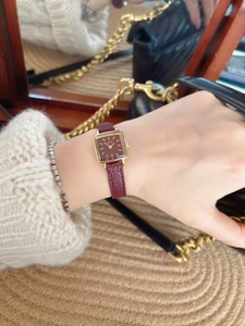 Detail of a vintage square gold watch with burgundy leather strap on a woven surface