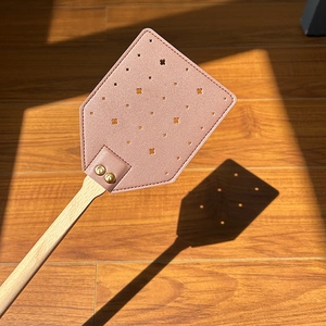 Pink floral faux leather fly swatter with a long ergonomic wooden handle on floor