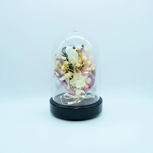 Detail of LED light strings wrapped around pink and white preserved flowers in glass dome