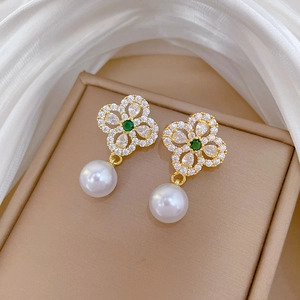 Detail of gold clover earrings with green stone and white pearl on jewelry box