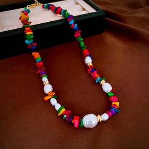 Close-up of colorful irregular stones and baroque pearls with gold clasp on dark fabric