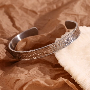 Detailed close-up of hammer textured silver stainless steel open bangle on stone