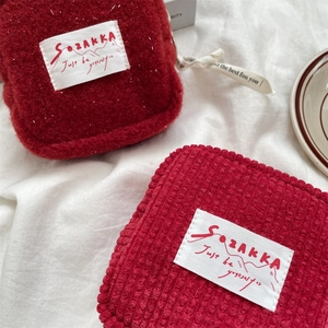 Detail of red plush storage pouch with brand label on a cozy white fabric background