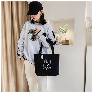 Detail of black corduroy tote bag with rabbit embroidery and cute cartoon pendant charm