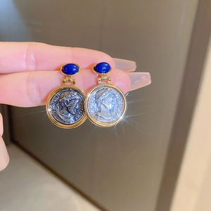 Close-up of vintage gold earrings with blue oval stones and embossed coin pendants
