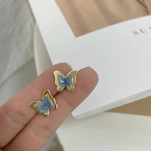 Detailed close-up of butterfly stud earring with blue marble inlay held by fingers