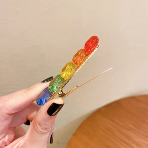 Golden hair clip with five colorful rainbow transparent resin gems held in hand