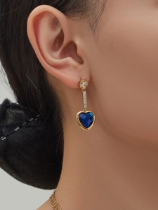 Detail of heart-shaped gold drop earrings with blue stone on female model