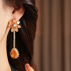 Close-up of golden floral earrings with large orange gems and crystals on a female model