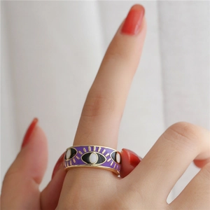 Detail of 18K gold plated evil eye ring with purple enamel finish on model finger