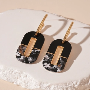 Detail of dark-style oval acrylic earrings with black and white marble patterns and gold frame