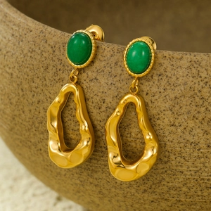 Detail of gold-plated geometric earrings with green stones on ceramic edge