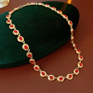 Détail macro du collier vintage doré serti de gemmes rouges sur velours vert