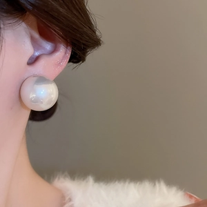 Gros plan d'une boucle d'oreille perle blanche surdimensionnée sur une oreille